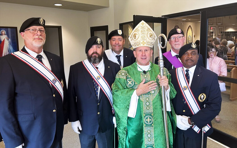 church leader in a green robe surrounded by Knights of Columbus