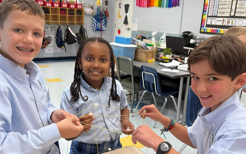 three students making a structure with spaghetti and marshmallows