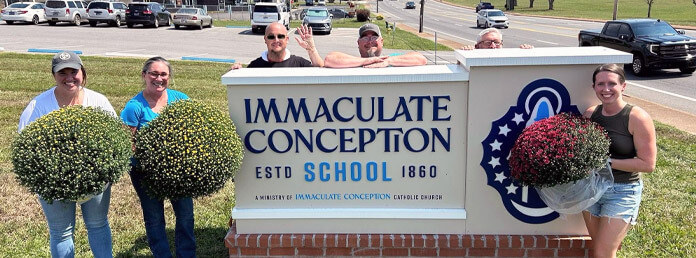 the IC school sign with people holding flowering shrubs