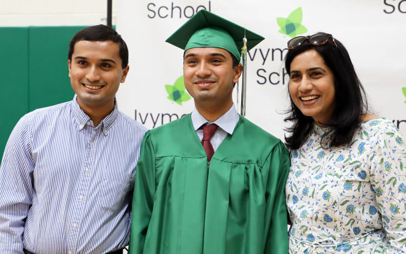 high school graduate in a green cap and gown with his parents on either side smiling