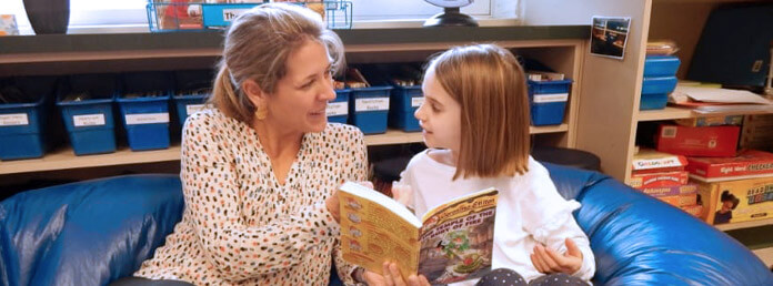teacher and student sitting on a blue beanbag reading a book