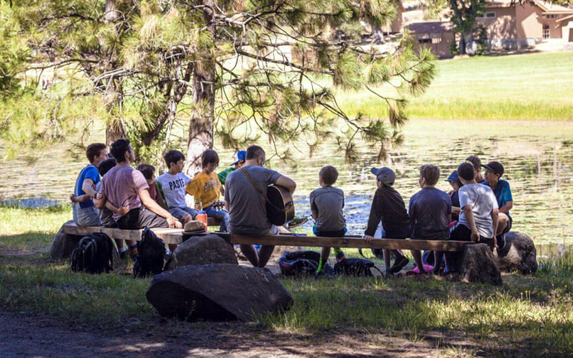 group of young boy campers singing while a counselor plays guitar
