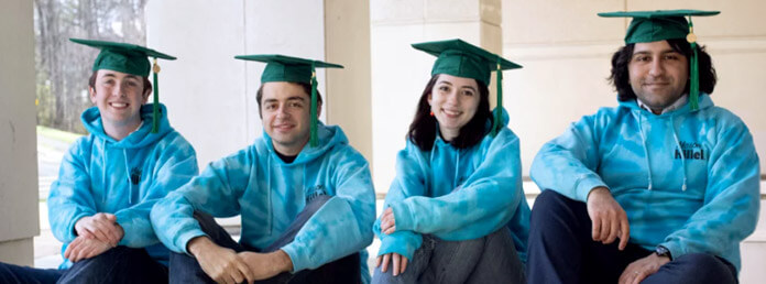 four students wearing blue sweatshirts and mortarboards
