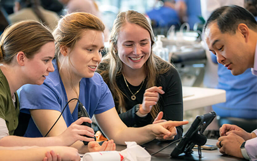 a professor talking to three students who are looking at a digital display