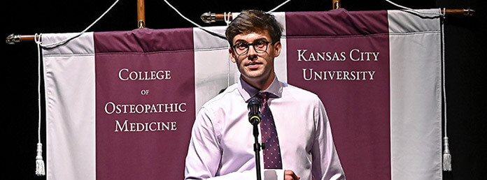 a speaker on stage in front of KCU banners