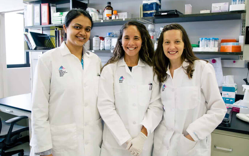 three researchers wearing lab coats smiling