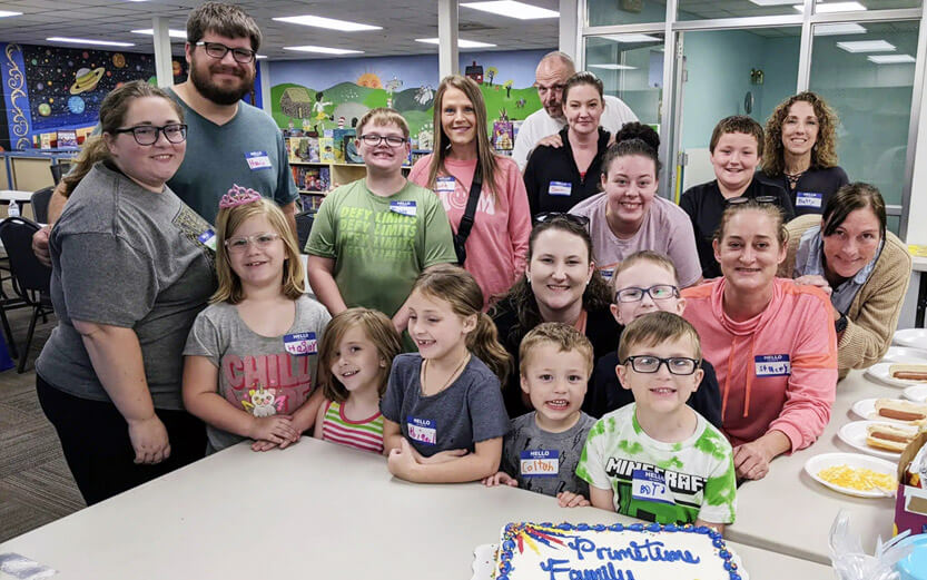 group of adults and kids behind a cake that reads Primetime Families