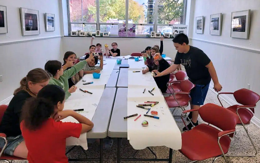 kids in a room around a table with arts and crafts supplies