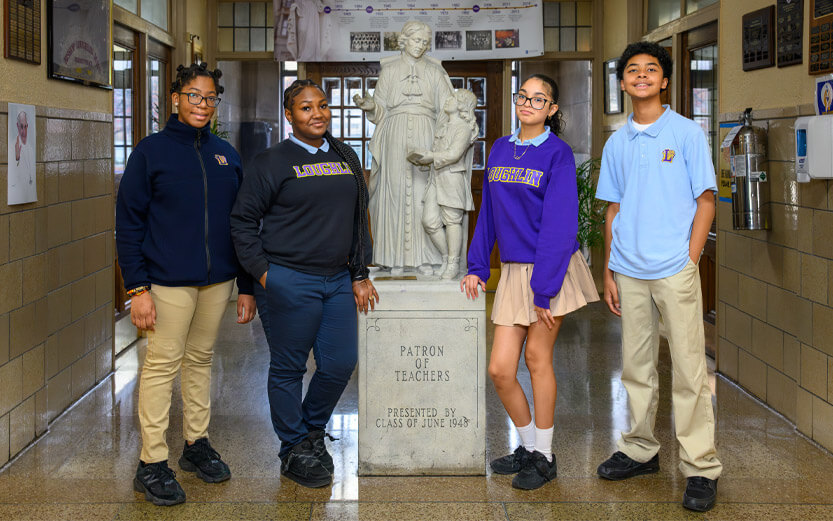 four students standing next to a statue inside a school building