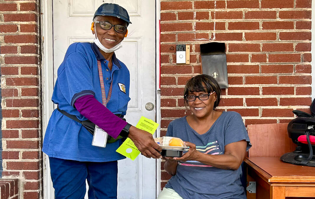 volunteer delivering a meal to a woman sitting on her porch