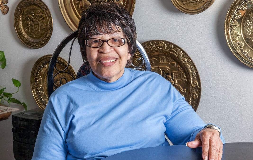 woman in a blue shirt sitting at her dining table smiling