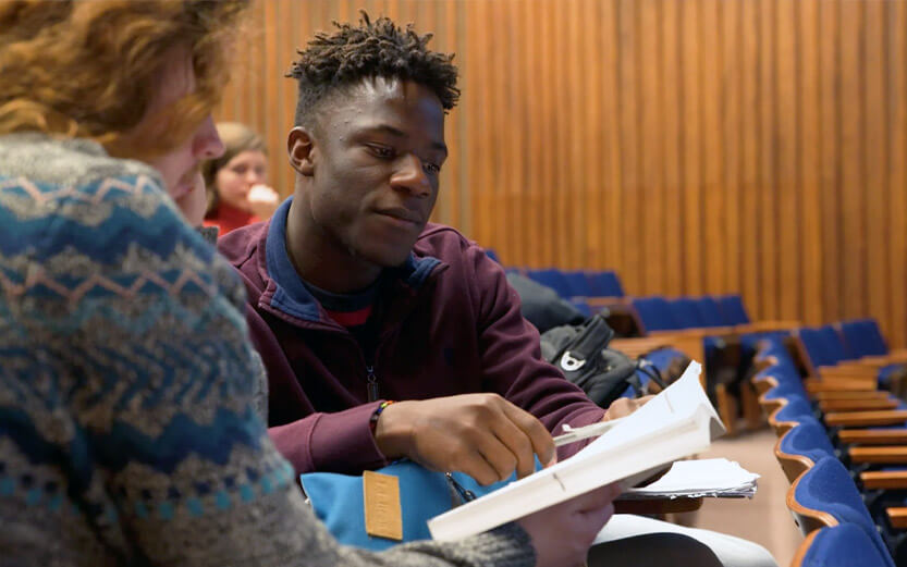 two students sitting in lecture hall looking at a paper together