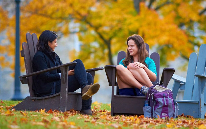 two female students sitting outside in adirondak chairs talking