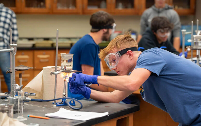 a chemistry student wearing goggles while operating a bunsen burner