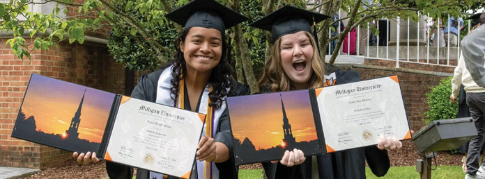 two female graduates smiling and showing off their diplomas