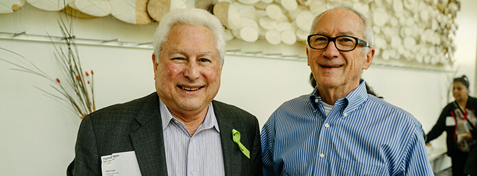 medium close-up shot of two older men standing side-by-side indoors