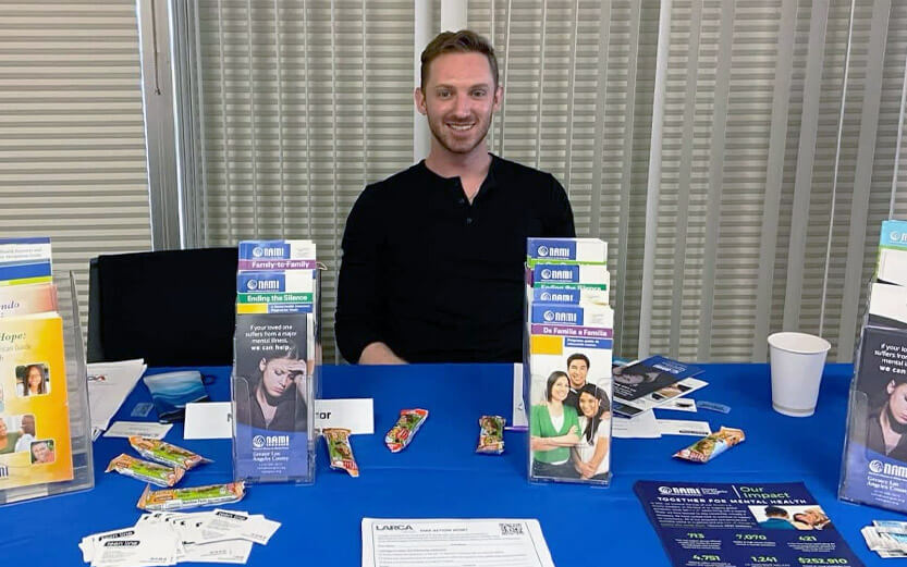 man sitting at an event table with NAMI brochures