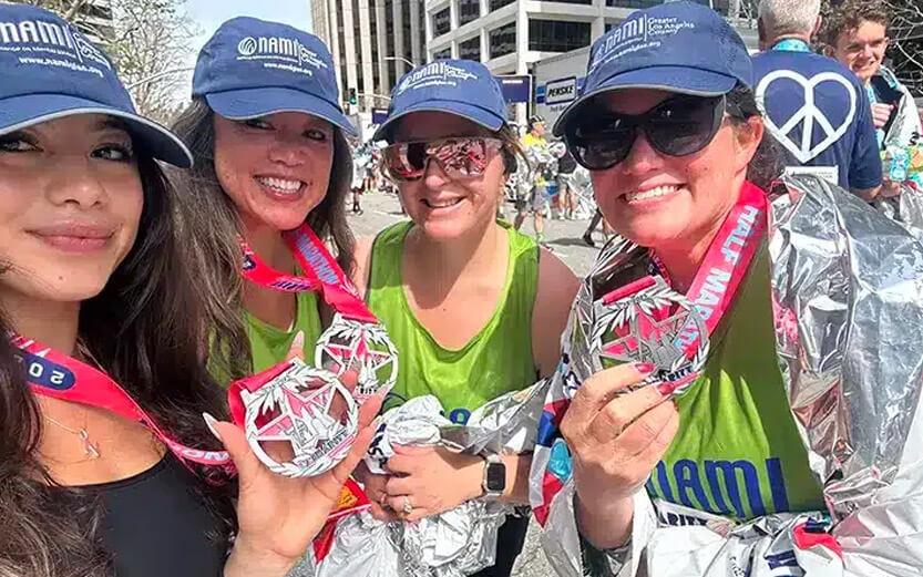 four LA Marathon runners wearing NAMI hats showing off their medals