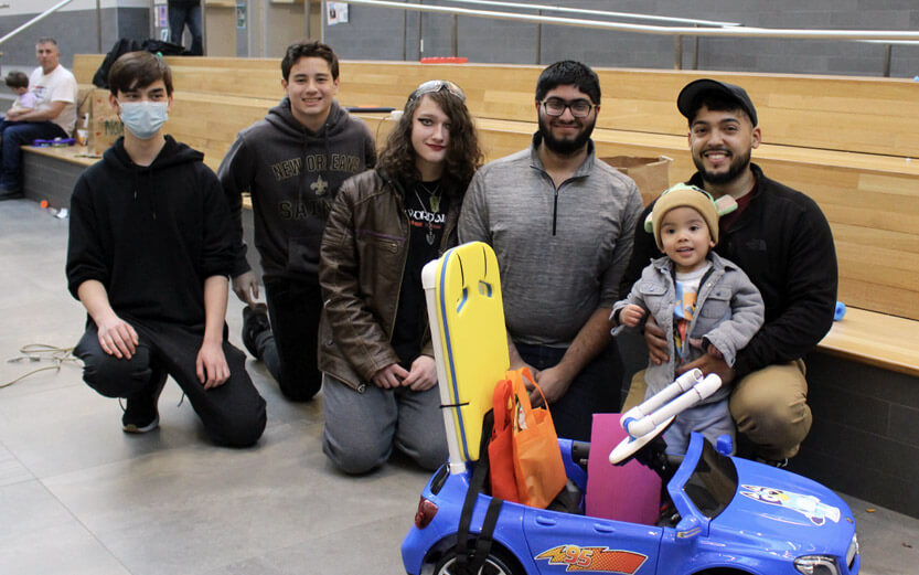 students kneeling with a toddler in front of their gobabygo car