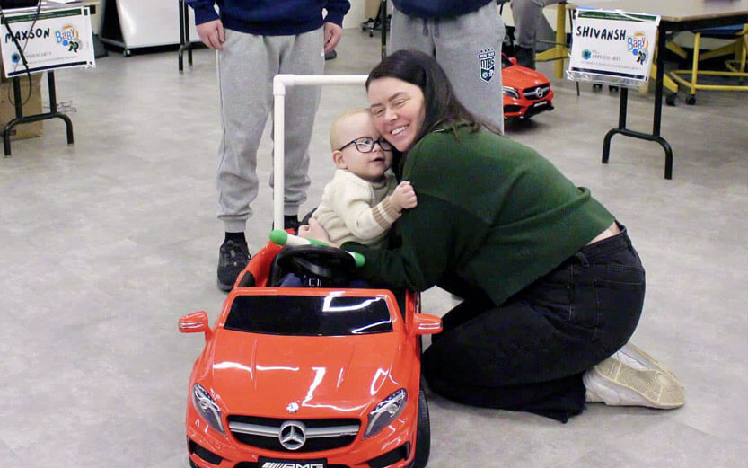 a toddler in a gobabygo car hugging a student