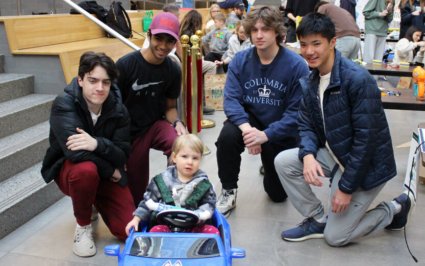 students kneeling behind a toddler in a gobabygo car