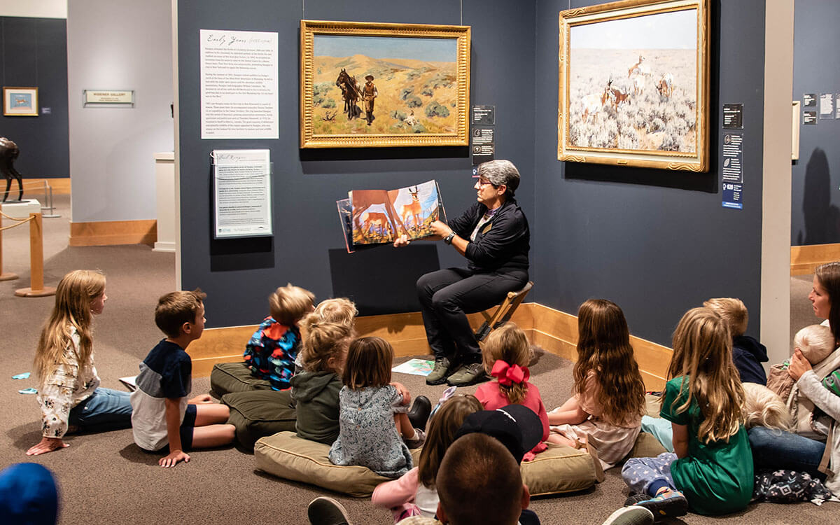 A woman sitting in a chair, reading a picture book to a group of children