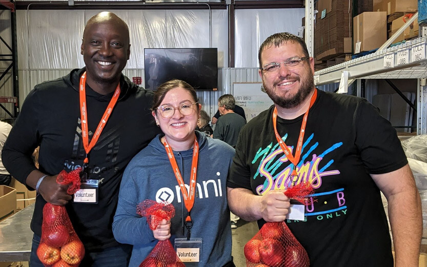 three food bank volunteers smiling and holding bags of apples