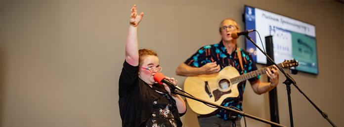 young girl singing with guitar player behind her