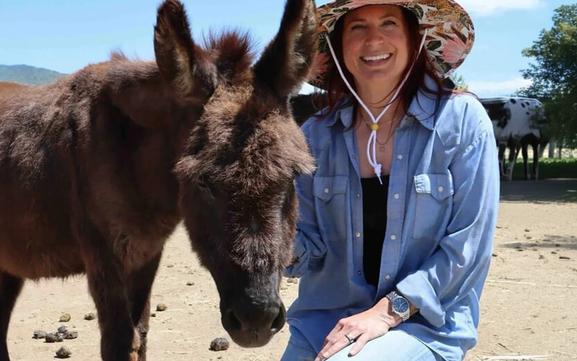 a volunteer smiling while petting a brown donkey