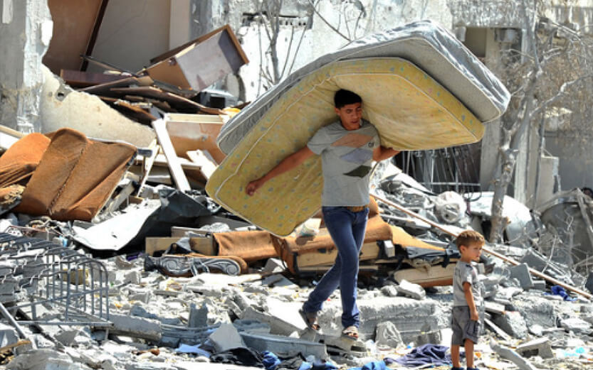 man carrying mattresses walking on rubble
