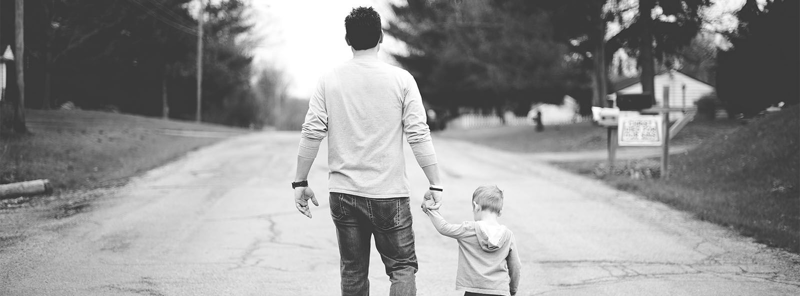 black and white photograph of a man walking down the street holding his young son's hand