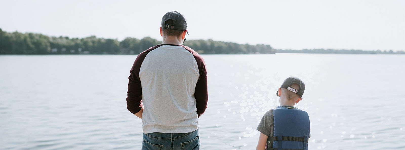 Man and son with their backs to the camera, at a lake