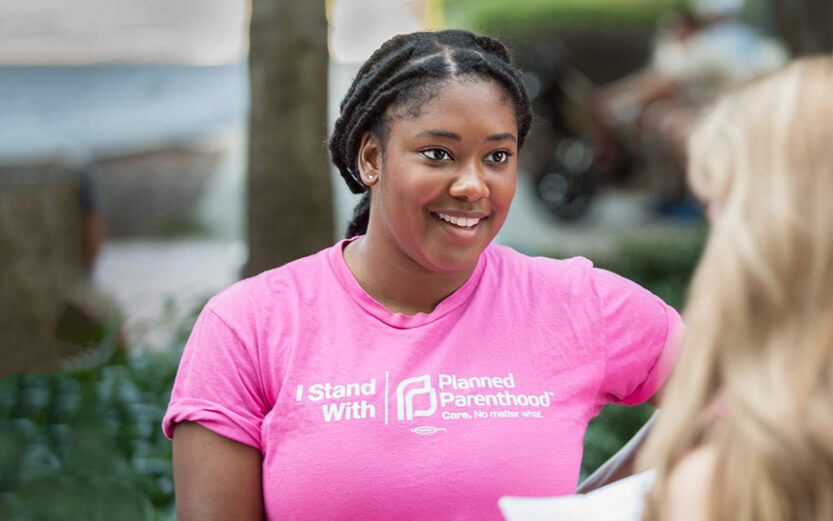 a Planned Parenthood volunteer wearing a pink t-shirt talking to a woman