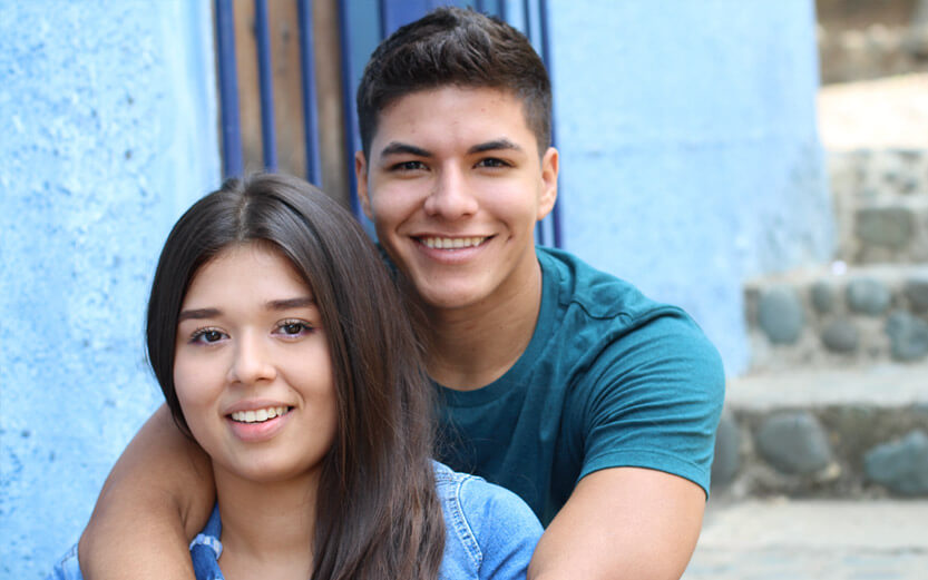a young latino couple sitting on steps smiling