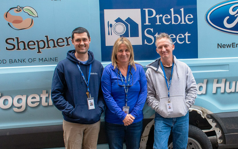 three volunteers standing in front of a food van smiling