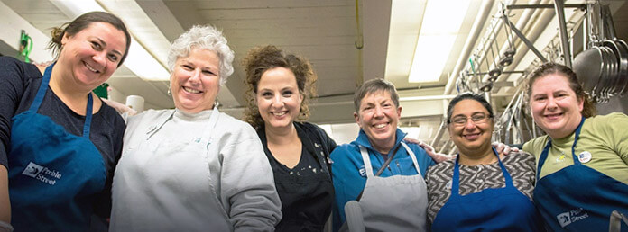 six food volunteers wearing aprons, smiling looking at the camera