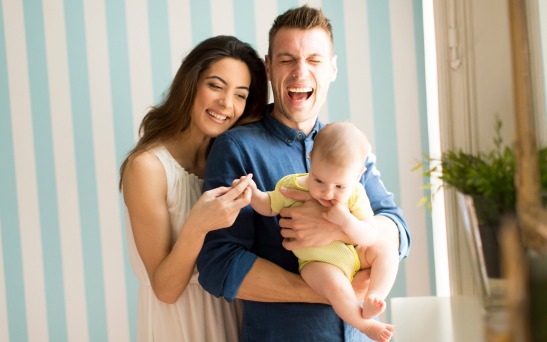 A mother and father laughing while holding their baby
