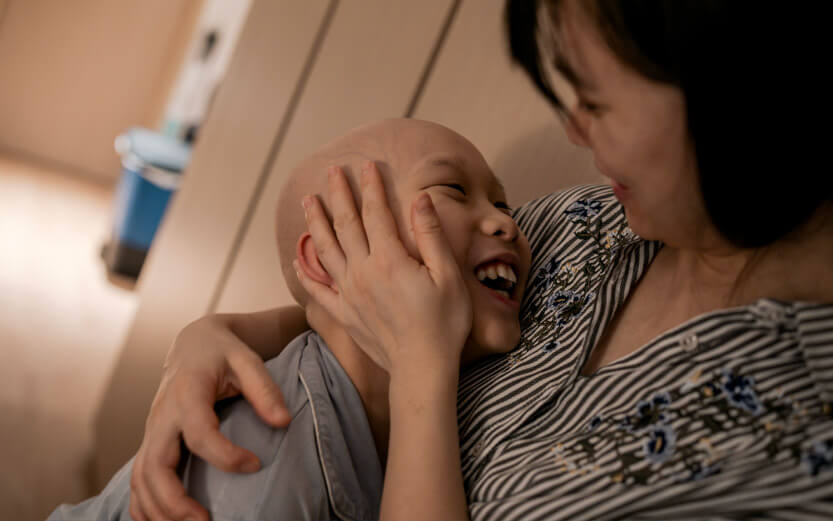 a child smiles and looks up at his mother who is hugging him