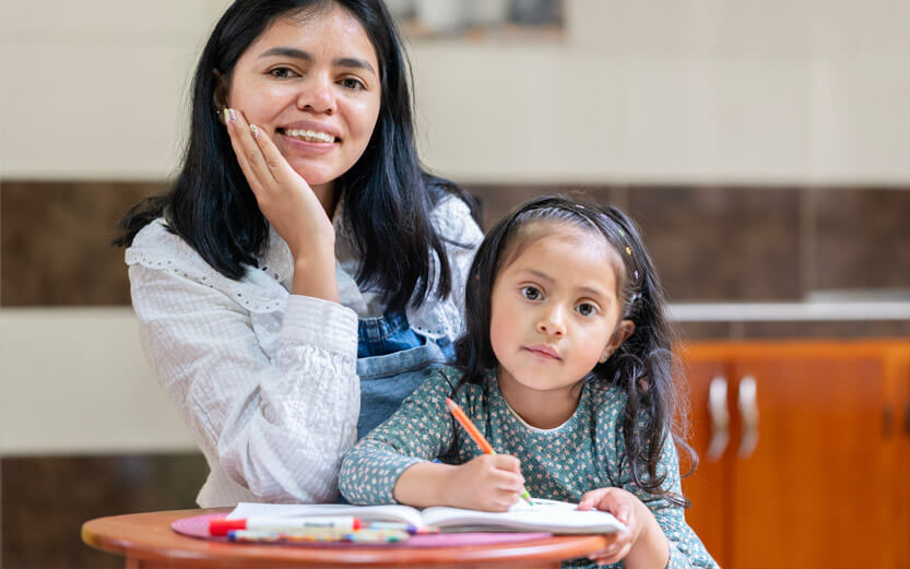 a mother sitting with her daughter who is writing in a notebook