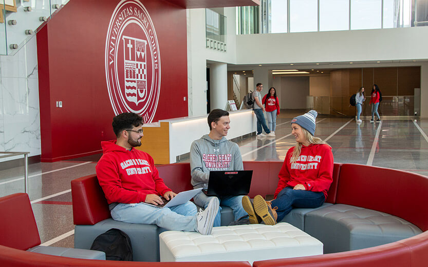 three students talking and studying in a school building lobby