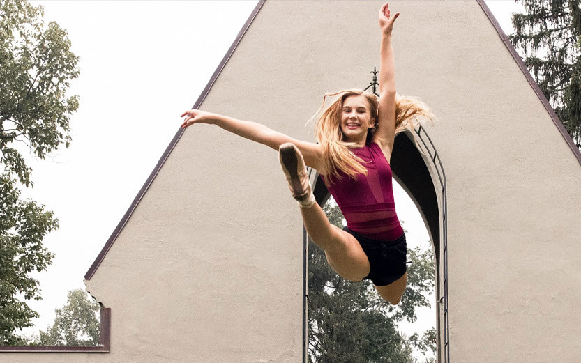 a dancer outdoors leaping into the air and smiling