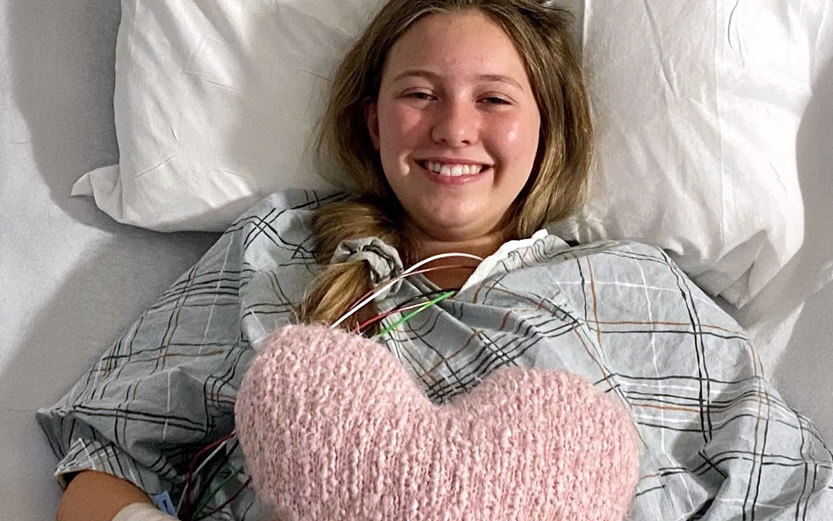 a teen girl in a hospital bed smiling and holding a pink stuffed heart