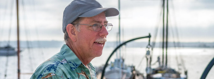 a senior man wearing a baseball cap and glasses with a marina in the background