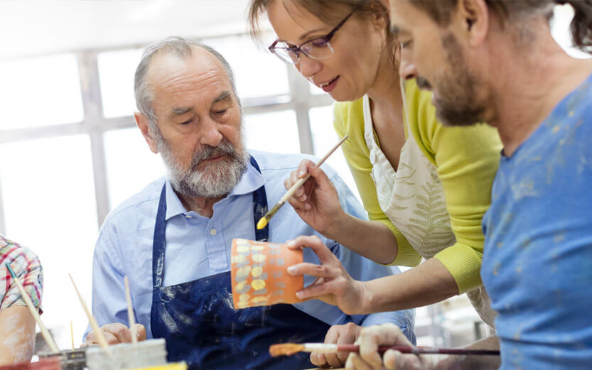 a senior man being helped by the teacher in a ceramics class