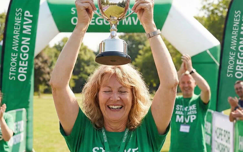 a woman wearing a green tshirt holding up a trophy smiling