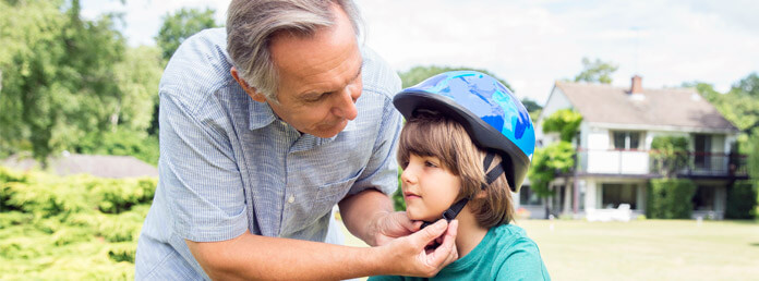a grandfather helping his grandson put on a bike helmet