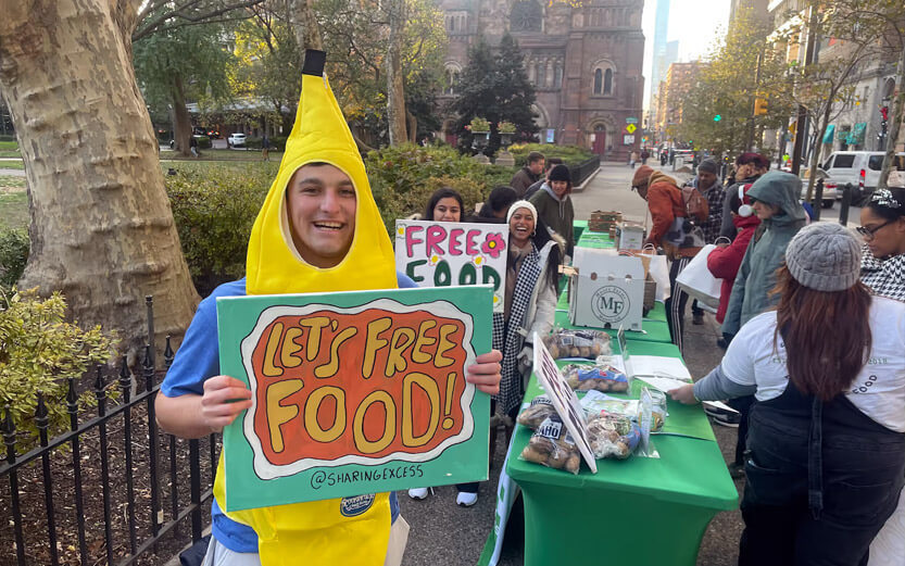 a volunteer dressed as a banana holding a sign that reads let's free food!