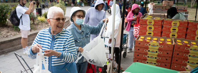 a senior woman laughing while talking to a volunteer at a food distribution event