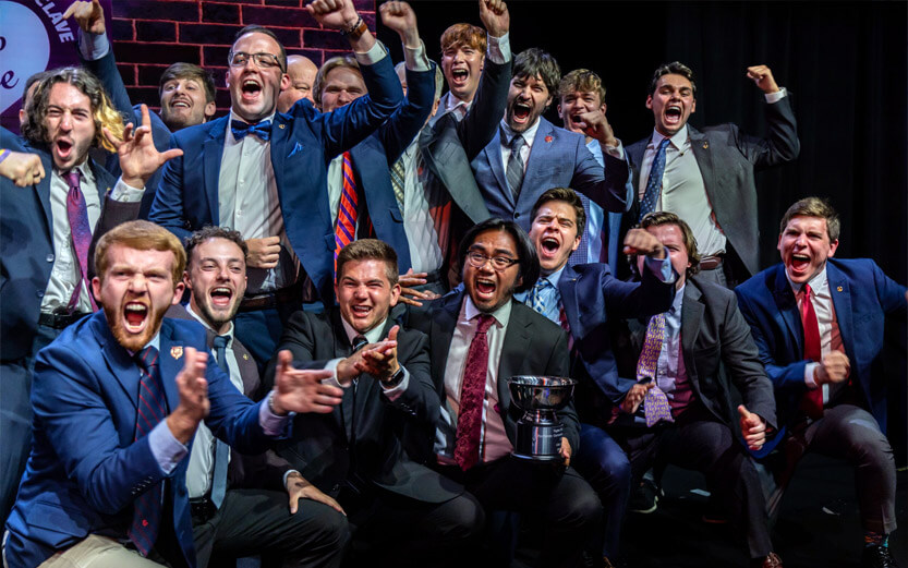 Sigma Phi Epsilon members wearing suits and cheering and showing off their trophy