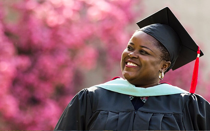 a graduate in cap and gown smiling big